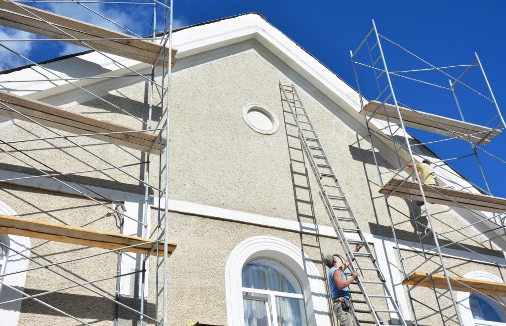 Painting and plastering exterior house scaffolding wall. Home facade insulation, stucco and painting works during exterior wall renovations and repair. Contractors plastering house facade outdoor